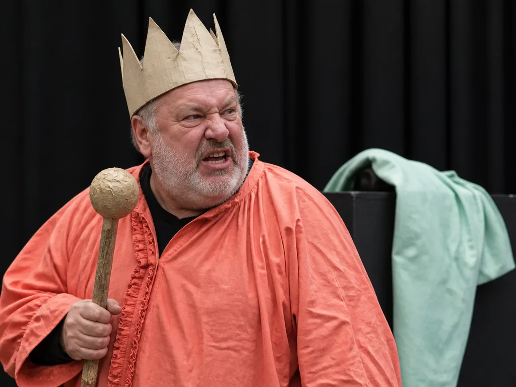 Le père Ubu, roi obèse et couronné, agite un sceptre sur une scène de théâtre
